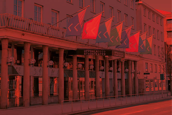 Fasadbild av Uppsala Stadsteater med färgglada flaggor